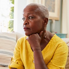 Senior woman in yellow shirt sitting on couch looking concerned