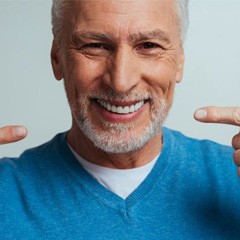 a man smiling and pointing at his new dentures