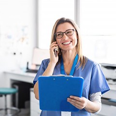 smiling dental team member talking on the phone and holding a clipboard