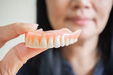 Close up of woman holding denture in Naples, FL