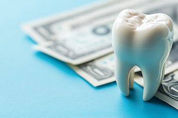 Large model tooth next to dollar bills on blue surface