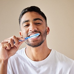 Man in white shirt smiling while brushing teeth