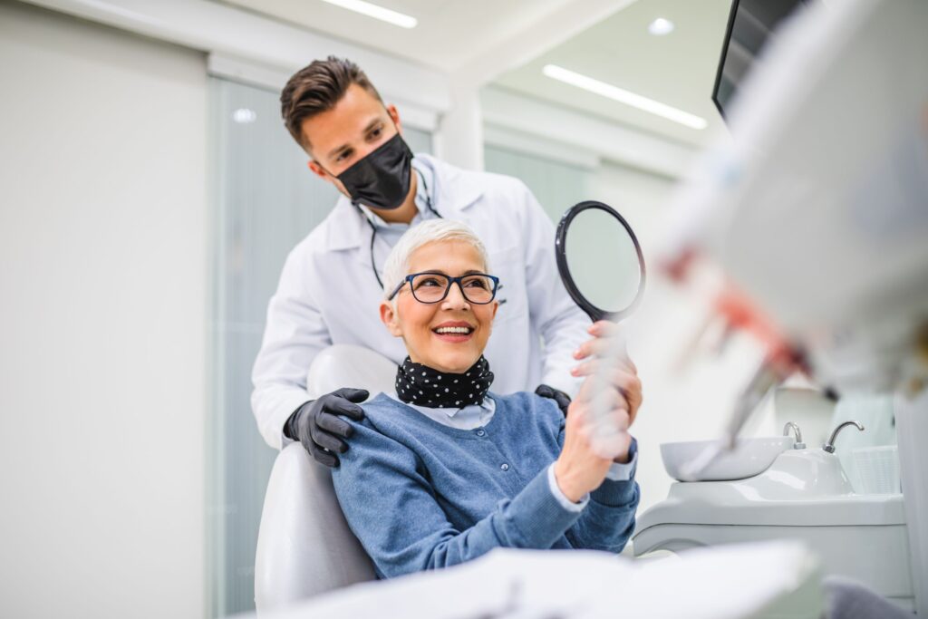 Woman in dental chair smiling at reflection in mirror with dentist touching her shoulders