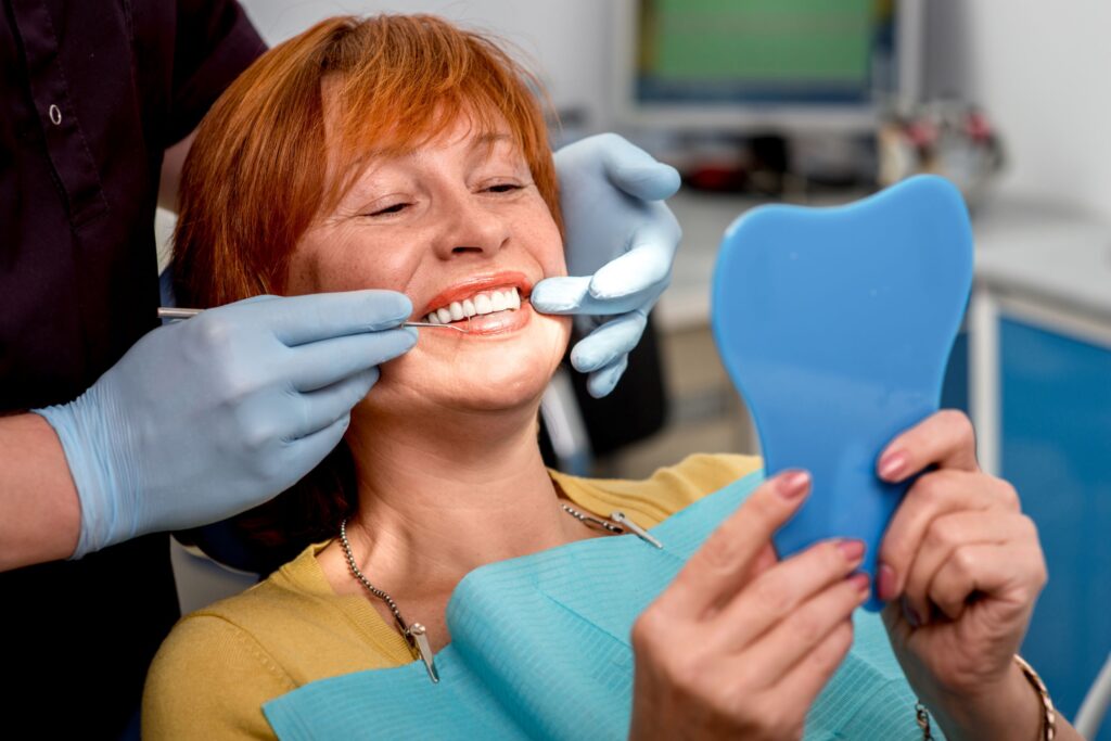 Woman with red hair looking at mirror as dentist touches her teeth
