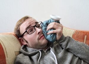 Man wearing glasses and holding cold compress to his face.