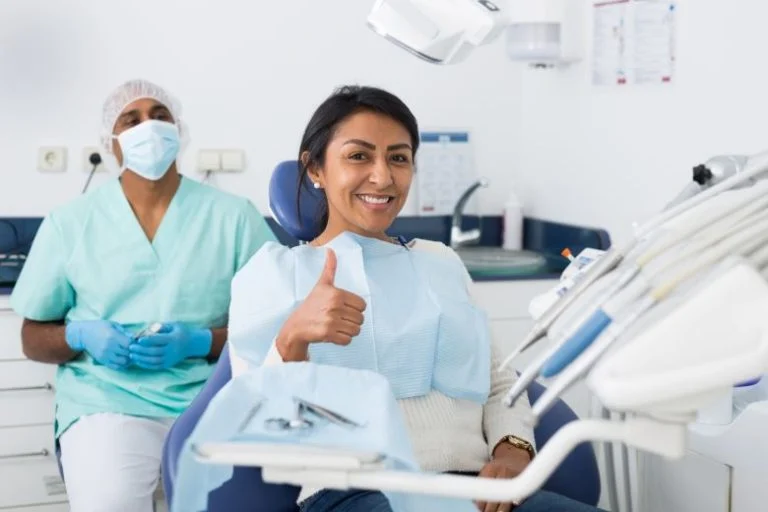 Patient giving a thumbs up in the dental chair beside an assistant
