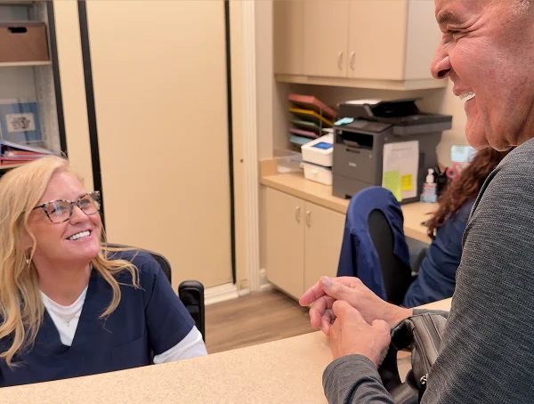 Dental team member in navy scrubs smiling at a patient at the front desk