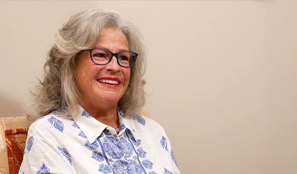 Smiling older woman with gray curly hair and glasses in a patient video testimonial