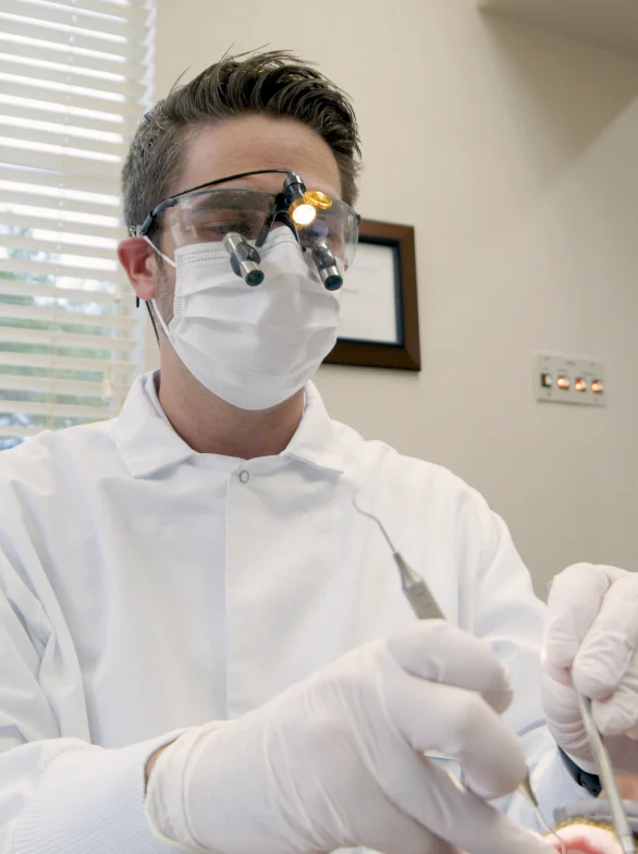 Dentist wearing a mask and magnifying loupes treating a patient