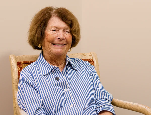 Smiling older woman in a blue striped blouse seated in a chair
