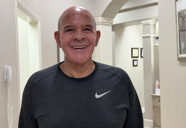 Smiling patient with a shaved head in a dark athletic shirt in a bright office